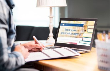 Kalem ve kağıt ile kolej veya üniversite başvuru formu yazma genç adam. Uygulama veya belge doldurma öğrenci. Burs, grant veya giriş. Laptop okul web sitesi.