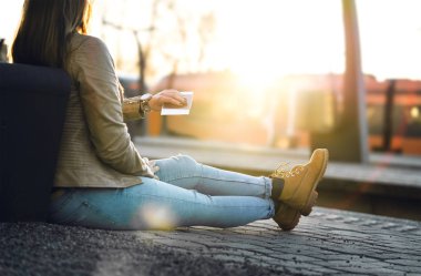 Bayan arıyorum zaman ve saat tren istasyonunda. Biletin ve pasaportun platformu ile oturan kadın. Güzel gün batımı ve güneş ışığı.