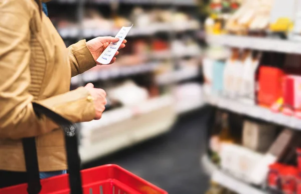 Reading shopping list in supermarket. Female customer in grocery store with budget, plan or checklist. Lady doing groceries and buying food for family. Shopper with basket between shelves in aisle.