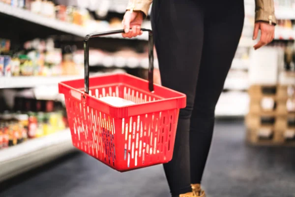 Woman holding shopping basket and walking in grocery store aisle. Lady buying groceries and food in supermarket or gourmet shop.