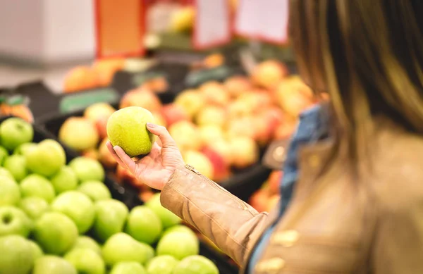 Shopping for fruit and healthy food in supermarket. Fitness lady on organic diet doing groceries. Woman buying, holding and choosing fresh apple in grocery store.