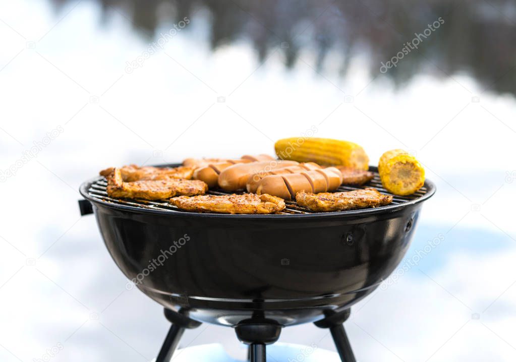 Grilling at the beach. Food cooking on a charcoal kettle grill. Sausages, meat, corn and vegetables in outdoor barbeque in summer. BBQ party, cookout or camping concept.