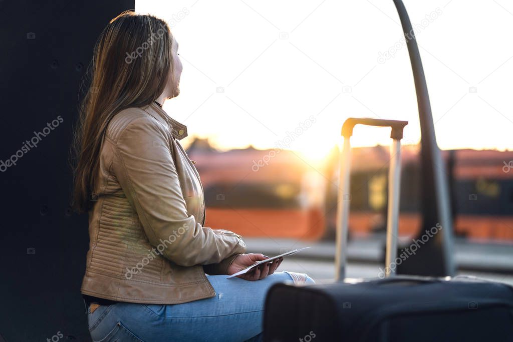 Lady sitting and waiting for train in station. Woman in platform at sunset with suitcase, ticket and passport.