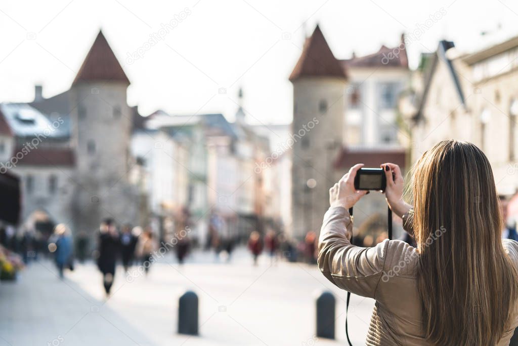 Tourist in Tallinn taking photo of Viru Gate. Woman on vacation taking picture of landmark in Estonia. People walking in popular street. Back view of girl with camera.