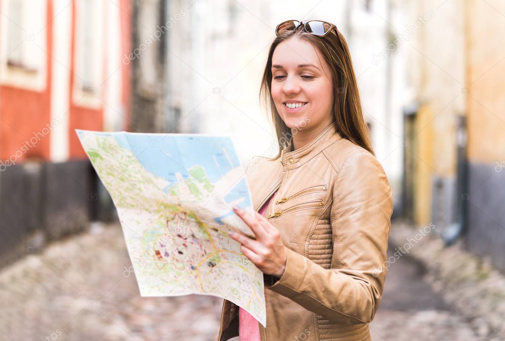 Happy young woman reading map. Smiling traveler navigating and planning sightseeing tour in city. Person on vacation in old town. Travel and navigation concept. Cheerful tourist looking directions.