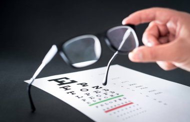 Gözlükçü holding gözlük. Görme test grafik içinde belgili tanımlık geçmiş. Sabitleme ve gözlük veya lens onarma göz doktoru. Optometrist veya klinikte çalışan göz doktoru.