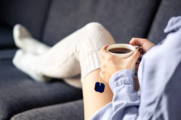 冬天穿着舒适温暖袜子的女人喝一杯茶 舒适的家 周末早上放松 这个季节流行的时尚风格 女孩躺在舒适的沙发上 感冒和流感的健康治疗 — 图库照片