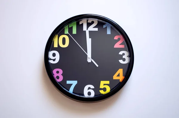 Clock on a white background. A few seconds to midnight. Multi-colored numbers on the clock.