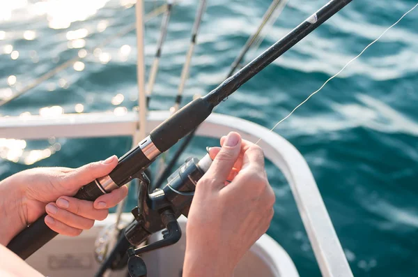 Female hand holding a fishing pole against the background of the sea. Sea fishing. The woman is fishing.