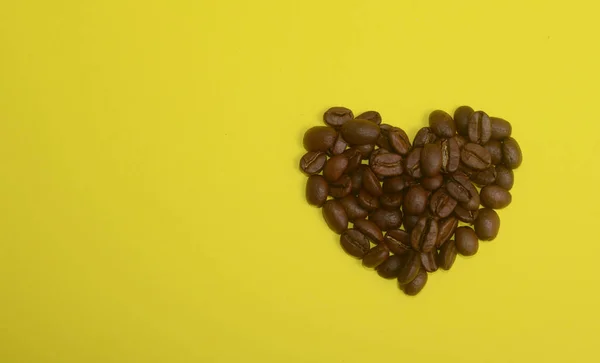 Szemes kávé, szív alakú, sárga háttér — Stock Fotó