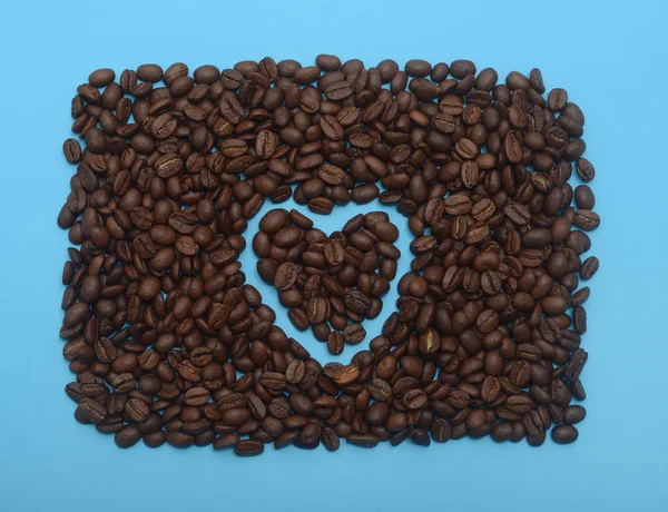 Grãos de café em forma de coração no fundo azul — Fotografia de Stock