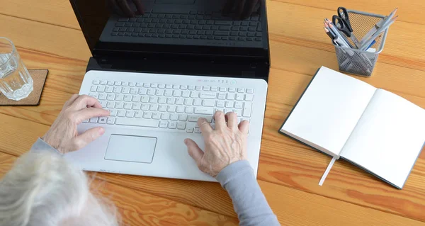 Egy idős asszony ül az asztalnál, és típusú laptop. — Stock Fotó