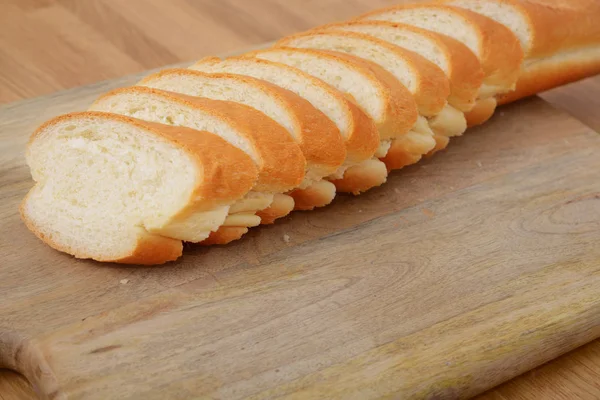 Scheiben französisches Brot auf Schneidebrett auf Holztisch — Stockfoto