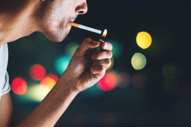 Gece dışarıda sigara yakan bir adamın yakın çekimi.