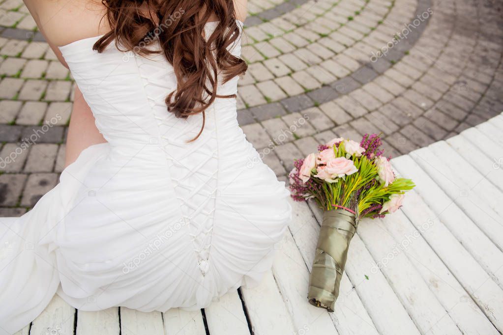 girl in a wedding dress sits on a stone bench with her back to the camera