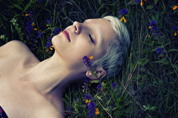 portrait of a young blonde girl lying on a forest grass