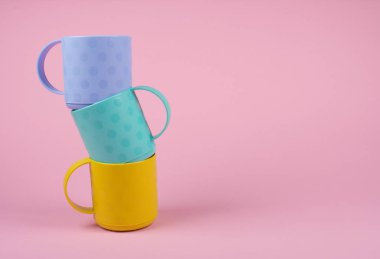 Pastel pembe arka plan üzerinde renkli bardak yığını