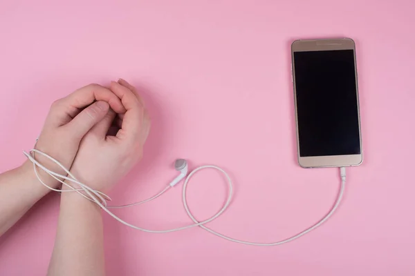 Mãos atadas com um cordão de fones de ouvido e um telefone celular — Fotografia de Stock