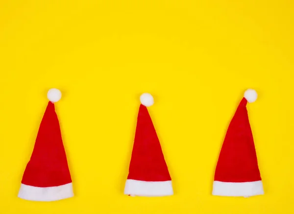 Três chapéus de Papai Noel no fundo amarelo brilhante — Fotografia de Stock