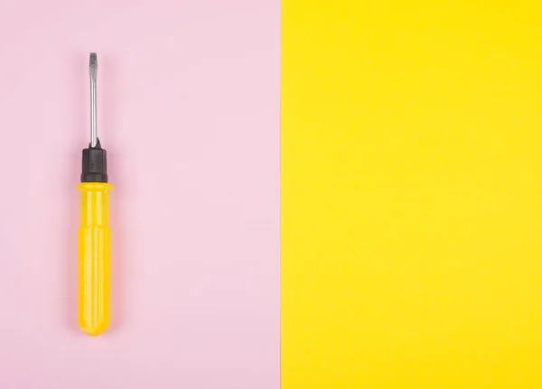 Yellow screwdriver on a split pink and yellow background — Stock Photo, Image