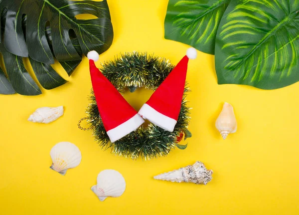 Chapéus de Papai Noel em uma grinalda de Natal, folhas tropicais e conchas — Fotografia de Stock