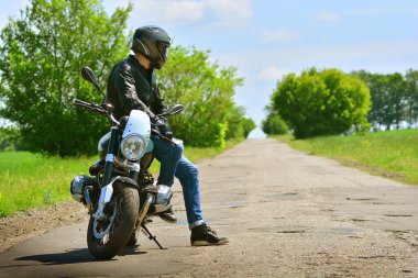 Stylish biker and his beautiful motorbike stoped on a abandoned road. Motorcycle background.  clipart