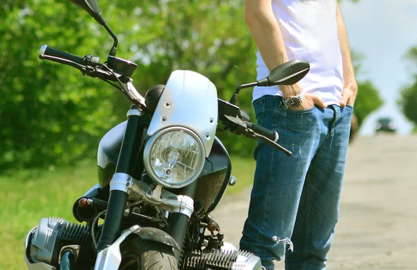 Motor bike lifestyle. Biker in white t-shirt and jeans near his motorcycle.