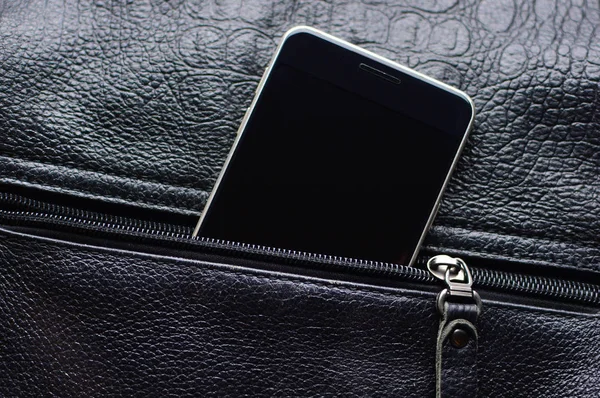 Black smart phone looks out from the unzipped leather pocket. Zipper and cell phone close-up with a place for the copy space.