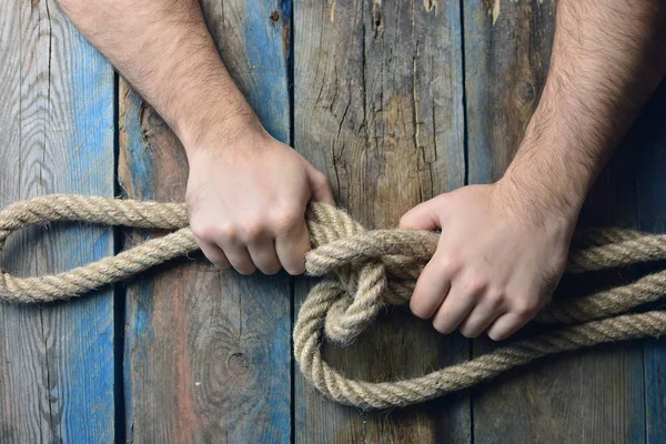 男性の手が木製の背景にロープの結び目をニットします — ストック写真
