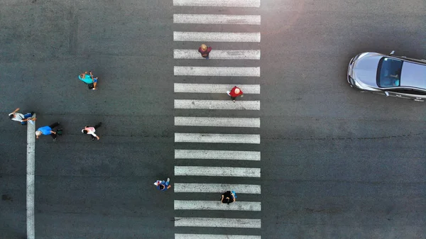 Aerial. Pedestrian crossing crosswalk. People group moving. Car stopped behind a crosswalk.