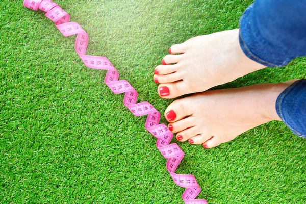 Fitness and diet concept with a woman legs and measure tape on a green artificial grass.