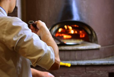Pizza maker in pizzeria makes pizza in wood-fired oven clipart