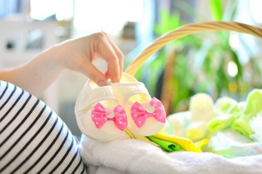 Hamile kadın evdeki doğum hastanesi için çanta hazırlıyor. Kız yeni doğan doğum için hazırlanıyor. Kadın elinde kız pembe booties.