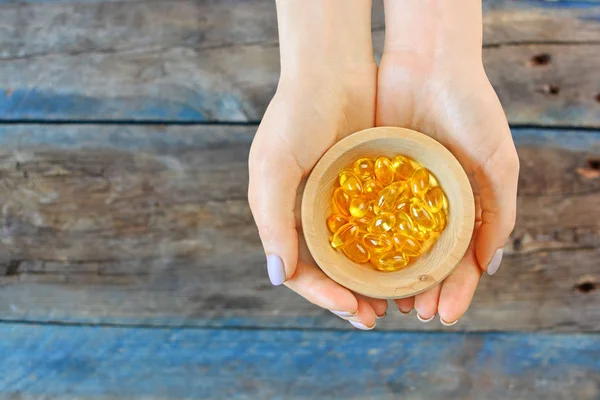 Natural Omega 3 vitamin capsules in a girl hands on a wooden background, copy space