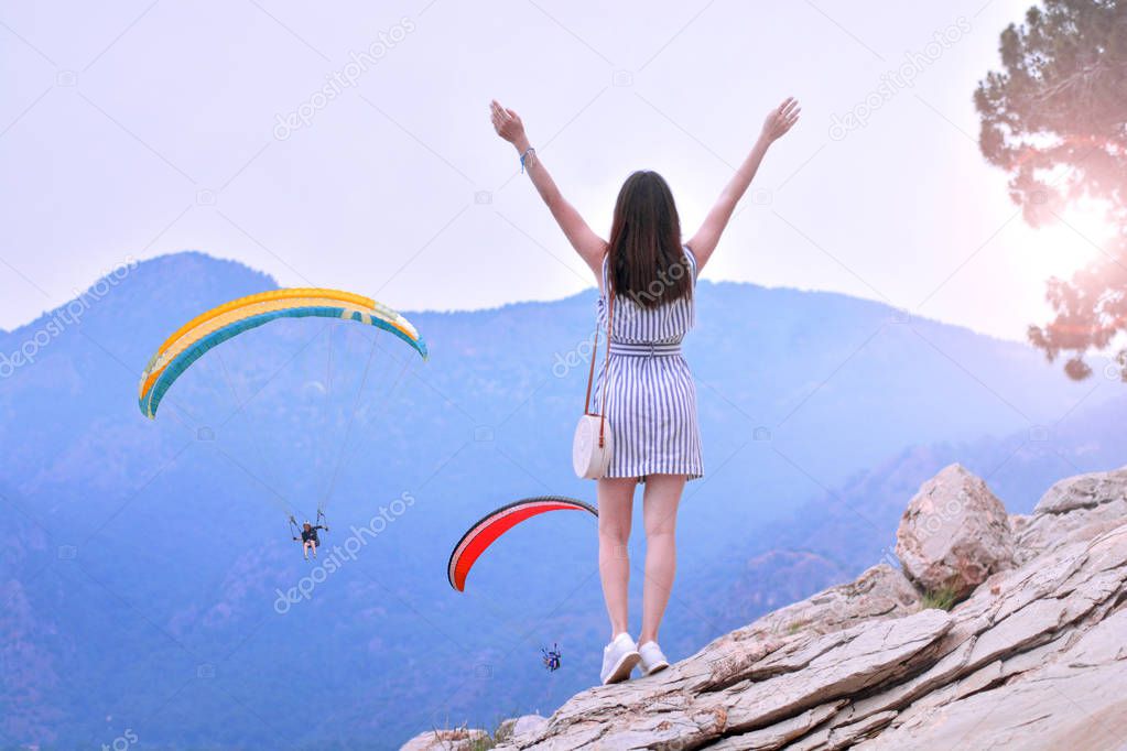 Happy girl takes hands up and enjoys beautiful mountain views with paragliding. She breathes in the fresh mountain air. Feeling fresh and freedom concept.