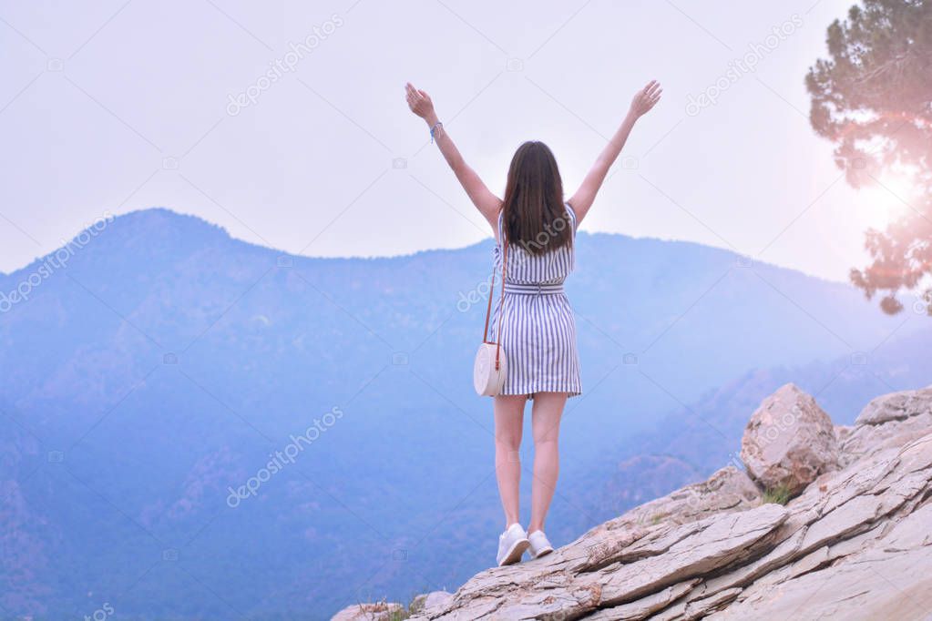 Happy girl takes hands up and enjoys beautiful mountain views. She breathes in the fresh mountain air. Feeling fresh and freedom concept.