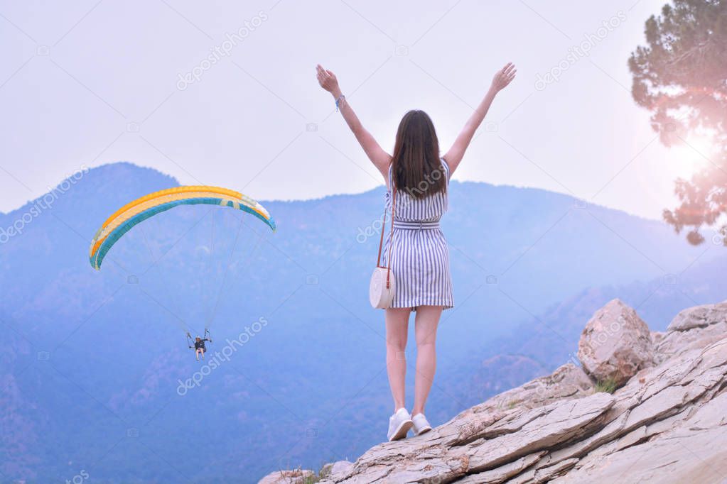 Happy girl takes hands up and enjoys beautiful mountain views with paraglider. She breathes in the fresh mountain air. Feeling fresh and freedom concept.