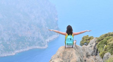 Happy girl with backpack takes hands up like a plane and enjoys beautiful sea and mountain view clipart