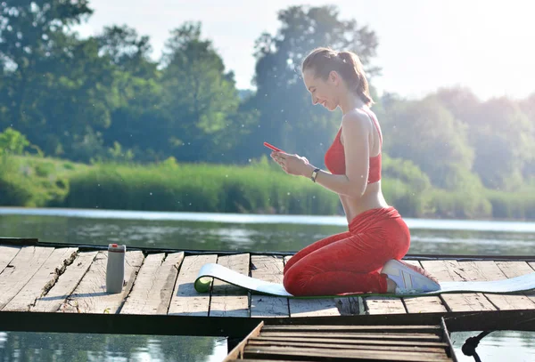 Healthy lifestyle background. Girl received a pleasant sms message during yoga on the fresh air outdoors.