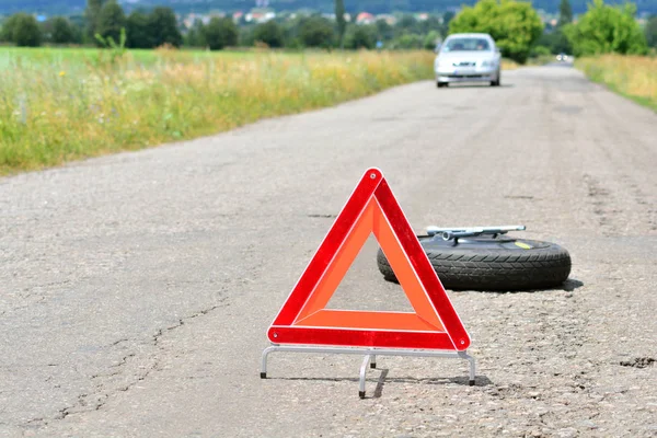 Red emergency triangle stop sign on the road. Spare wheel and wheel wrench on a backdrop. Oncoming traffic.