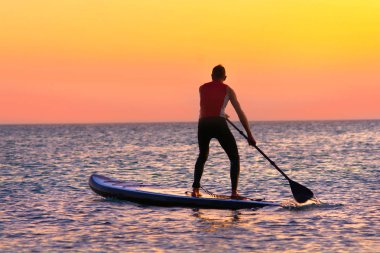 Gün batımında kürek yatılı ayağa kalkın. Sessiz bir denizde sup sörf yüzücü silueti. 