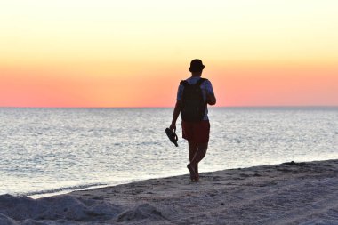 Turist deniz kıyısında yürür ve gün batımının tadını çıkarır