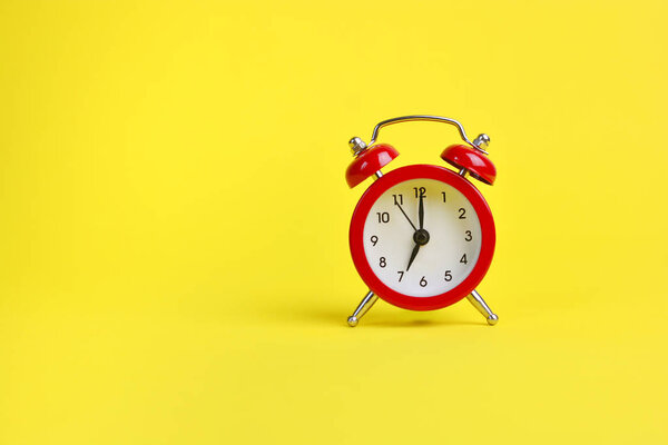 Red alarm clock on a yellow background. Copy space.