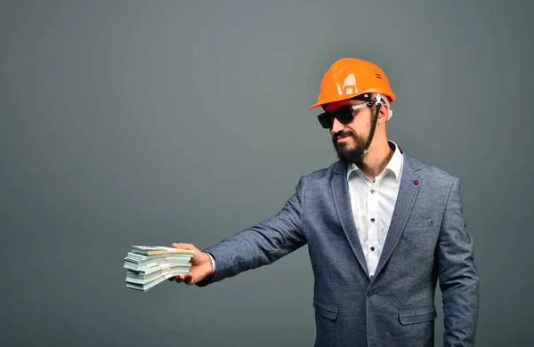 Serious general contractor or real estate investor in building helmet giving dollars cash.