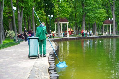 Parktaki göle bakıyorum. İşçi bir ağ ile gölü temizler. Kharkiv, Ukrayna - 25 Mayıs 2020.