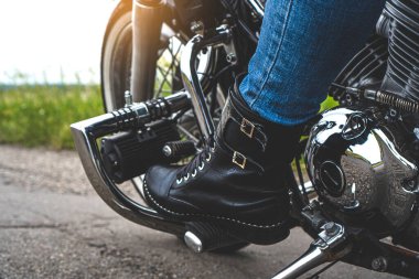 Deri çizmeli bir kadının bacağı motosiklet pedalında durur.