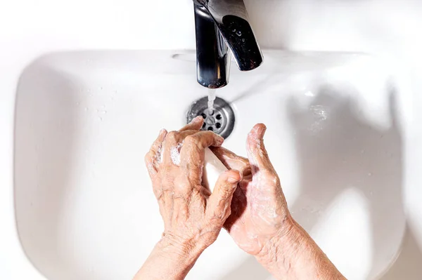 Elderly woman wrinkled hands washing. Hand hygiene to prevent infection. Take care of the elderly. View above.