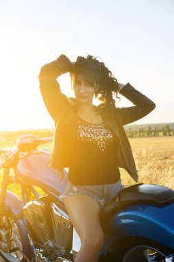 Motosikletli kız gün batımına karşı oturuyor..