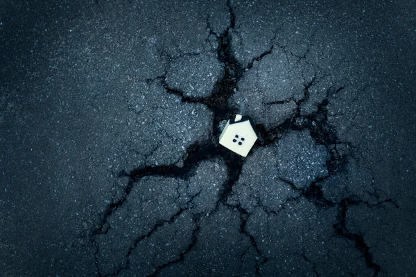 Kırık bir asfalt delikte küçük oyuncak evle konutların tahrip edilmesi kavramı.