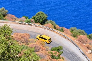 Car rental during the travel concept. Yellow car driving by the serpentine road over the sea. Beautiful mediterranean landscape. clipart